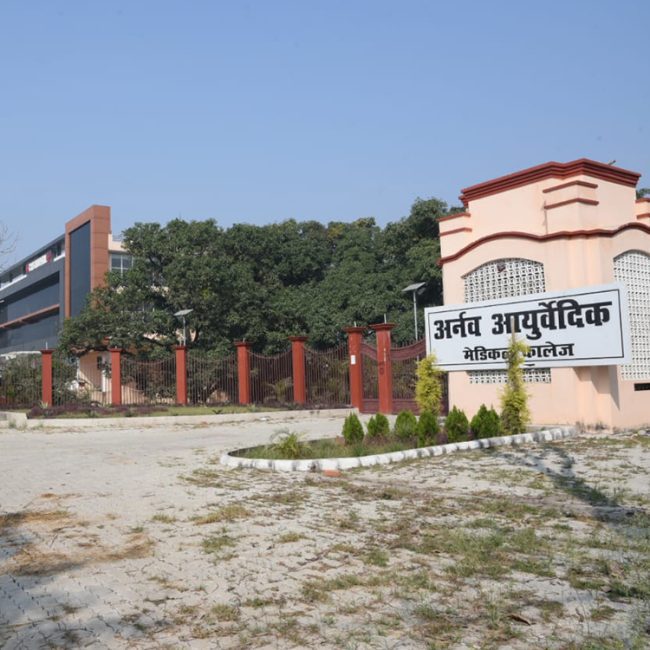 "Exterior view of modern Ayurvedic medical college building in UP featuring pink architecture with Hindi signage and well-maintained campus grounds"