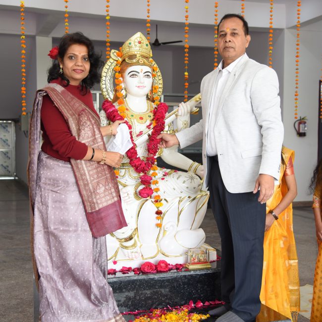 "Traditional Hindu ceremony at Ayurvedic medical college featuring decorated Hanuman deity statue with marigold garlands, conducted by faculty members in formal attire